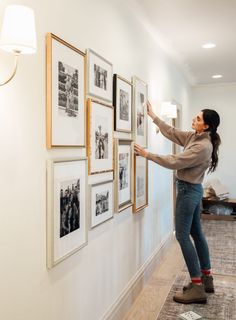 a woman standing in front of a wall with pictures on it and pointing at something