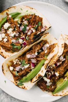 three tacos with meat, onions and green beans on a white plate