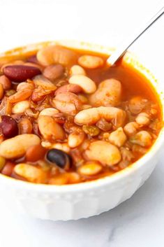 a white bowl filled with beans and other food on top of a table next to a spoon