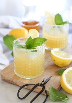 two glasses filled with lemonade and mint sit on a cutting board next to scissors