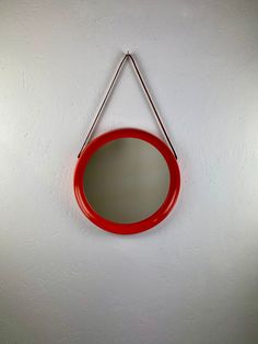 a red mirror hanging on the wall with a metal hook attached to it's side