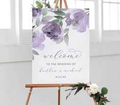 an easel with a welcome sign on it and flowers in the corner next to it