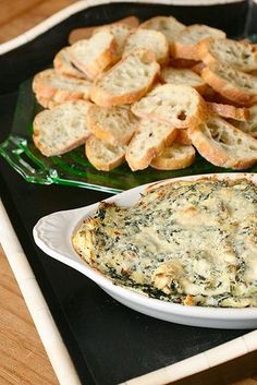 there is a bowl of spinach dip and crackers on the tray next to it