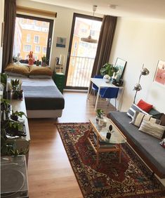 a living room filled with furniture and a large window next to a bed on top of a hard wood floor