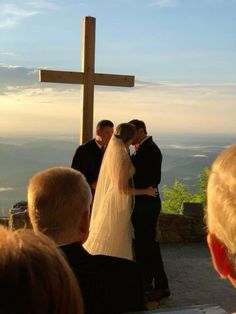 the bride and groom are getting married in front of a cross on top of a hill