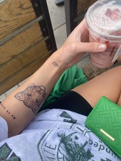 a woman with tattoos on her arm holding a cup of coffee and a green wallet