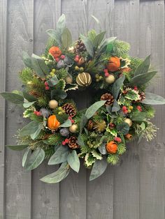 a christmas wreath hanging on the side of a wooden fence with evergreens, berries and pine cones