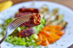 a fork with food on it is being held by someone's hand over a plate