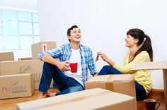 a man and woman sitting on cardboard boxes in an empty room with coffee mugs