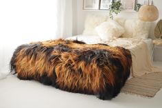 a bed with furry blankets and pillows in a white room next to a rug on the floor