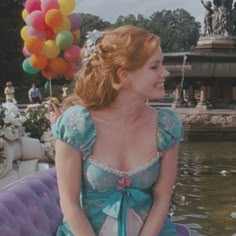 a woman sitting on top of a purple couch in front of a fountain with balloons floating over her head