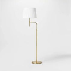 a gold floor lamp with a white shade on it's head and a round base