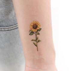 a small sunflower tattoo on the left inner arm and wrist, with green leaves