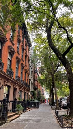 an empty city street lined with brownstone apartment buildings and trees in the foreground