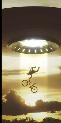 a man riding a bike through the air under a light that looks like a spaceship