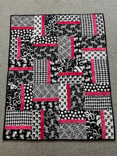 a black and white patchwork quilt with pink trims on it, sitting on the floor