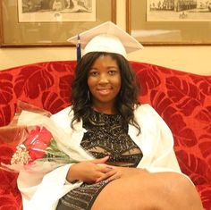 a woman sitting on top of a red couch wearing a graduation gown and holding flowers