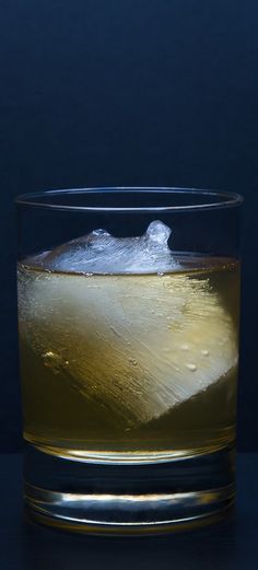 a glass filled with liquid and ice sitting on top of a table next to a blue wall