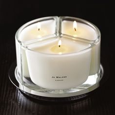 a white candle sitting on top of a wooden table next to a glass container with four lit candles in it