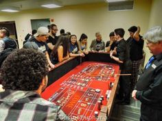 a group of people standing around a rouleette in a conference room with red cloth