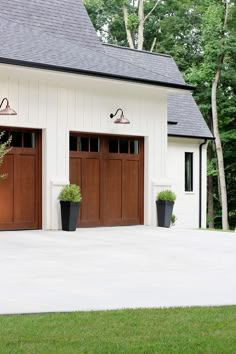 two brown garage doors on the side of a white building with black planters in front