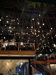 people are sitting at tables in a restaurant with lights hanging from the ceiling above them