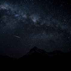 the night sky is filled with stars, and there are mountains in the foreground