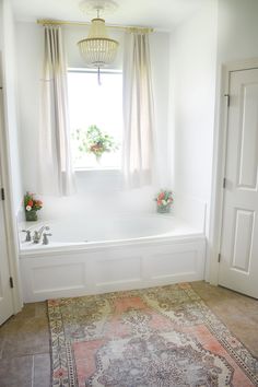 a bath tub sitting next to a window in a room with a rug on the floor