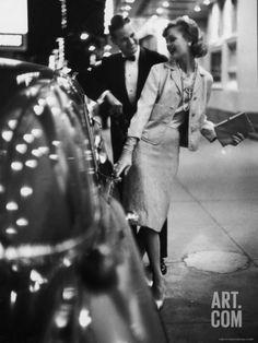 black and white photograph of woman standing next to fire hydrant on sidewalk with people walking by