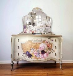 a white dresser with flowers painted on it and a mirror over the top that is sitting on a hard wood floor