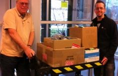 two men standing next to each other in front of boxes on a dolly with yellow caution tape