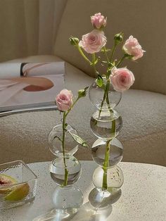 three clear vases with pink roses in them on a table next to a book