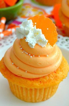 a cupcake with orange frosting and white sprinkles on top is sitting on a table