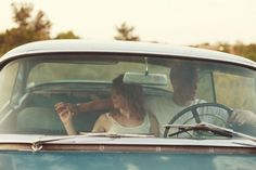 a man and woman sitting in the driver's seat of a blue vintage car