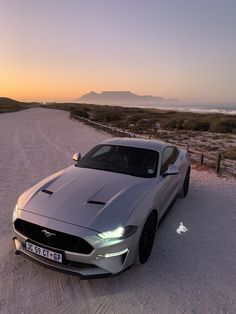 a silver sports car parked on the beach at sunset