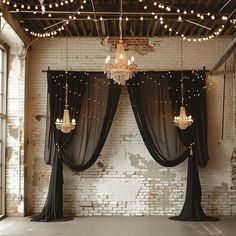 an empty room with black drapes, chandelier and lights hanging from the ceiling