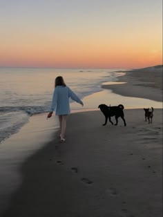 the woman is walking her dogs on the beach at sunset or sunrise, and there are footprints in the sand