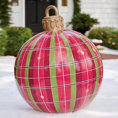 a red and green ball ornament sitting on top of snow in front of a house