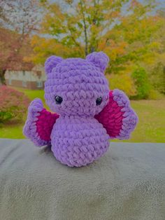 a purple crocheted stuffed animal sitting on top of a blanket in front of trees