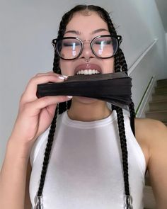 a woman wearing glasses and holding up a piece of black material to her face with long braids