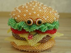 a close up of a toy hamburger with googly eyes and beaded beads on it