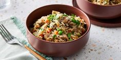 two brown bowls filled with rice and vegetables next to silverware on a white table