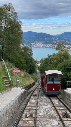 a red train traveling down tracks next to a lush green hillside and lake in the distance