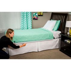 a woman kneeling on the floor in front of a bed with a green bedspread