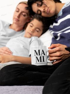 two women and a child laying on a bed holding a coffee mug