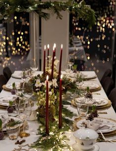 the table is set for christmas dinner with candles and greenery on each place setting