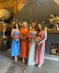 four bridesmaids pose for a photo in front of some wine barrels and flowers