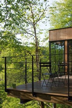 a wooden deck in the woods with chairs and table on it, overlooking a wooded area