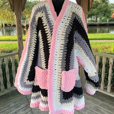 a crocheted coat is hanging on a wooden porch