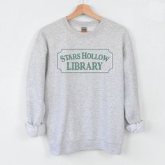 A cozy crewneck for our favorite fictional library! This sweatshirt belongs in your GG collection and pairs perfectly with our Stars Hollow Books tote or tee. • 50% polyester, 50% cotton• Pre-shrunk for extra durability• Regular fit • For size guide, view 3001 Tee See all of our bookish sweatshirts and bookish hoodies Stars Hollow Library, Stars Hollow Books, Bookish Sweatshirts, Gg Collection, Hollow Book, Ash Gray, Girl House, Comfort Colors Tee